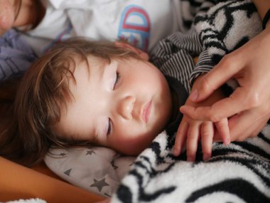 Uyuyan anne uyuyan bir bebeğe sarıldı. Anne ve küçük oğlu büyük bir yatakta uyur, battaniyenin altında saklanırlar..