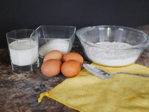 Υλικά για το ψήσιμο ζύμης. αλεύρι, αυγά, γάλα. Υλικά ψησίματος. Κουτάλι σε μαρμάρινο τραπέζι. Προετοιμασία για μαγείρεμα. — Φωτογραφία Αρχείου