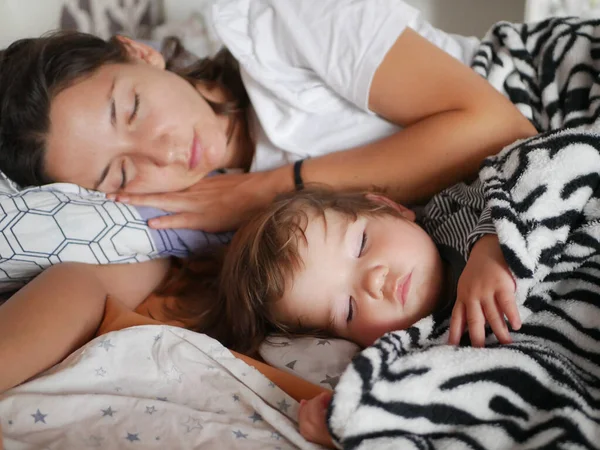Dítě spí s mámou v posteli. Roztomilý chlapec a jeho matka leží v ložnici na pohovce a přes den klidně spí. Bezpečný spánek dítěte a matky. — Stock fotografie