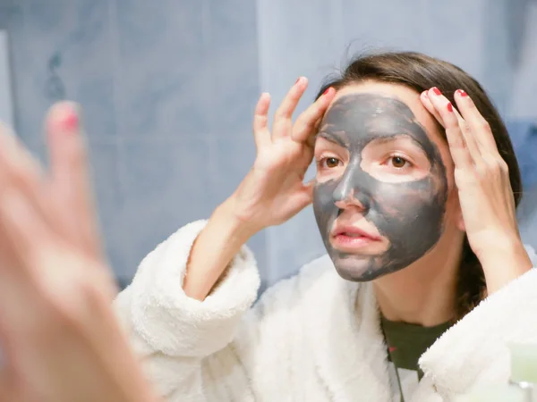 Girl cares for oily skin. Cosmetic procedures. Skin care. Young woman with a black mud mask on her face. cleansing pores. Cosmetic procedures. — Stock Photo, Image