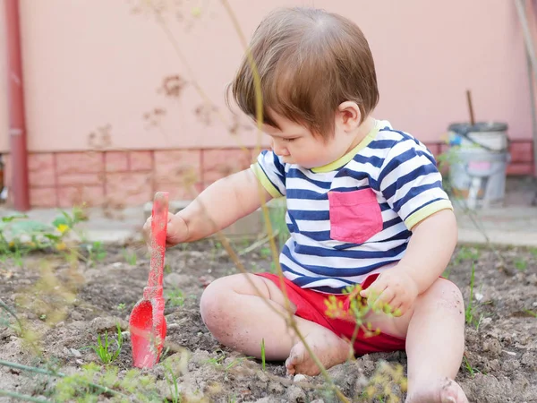 Un garçon joue avec une spatule dans la rue. Petit garçon et pelle rouge. Garçon 0-1 ans — Photo