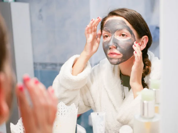 Menina e máscara facial. Mulher com máscara preta de argila carbo no rosto. A menina cuida da pele oleosa. Procedimentos estéticos. Cuidados da pele . — Fotografia de Stock