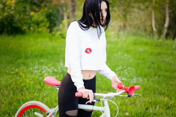 Meisje op een rood-witte fiets. Een mooi jong sexy gebruind atletisch meisje rijdt in de natuur. Vrolijk en lachend brunette. goede cijfers. — Stockfoto