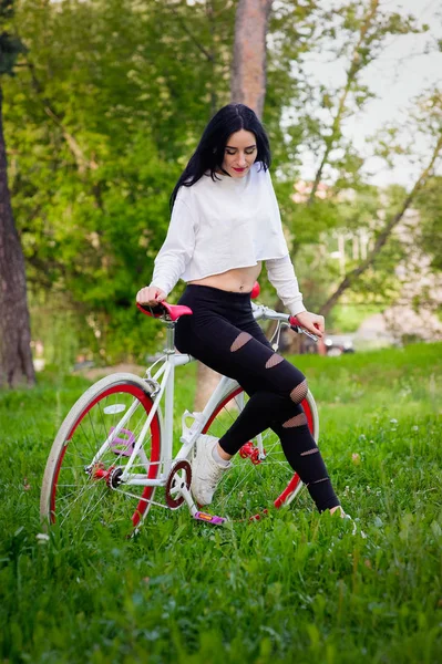 Chica en una bicicleta roja y blanca. Una chica atlética bronceada sexy bastante joven cabalga en la naturaleza. morena alegre y sonriente. buenas cifras . — Foto de Stock