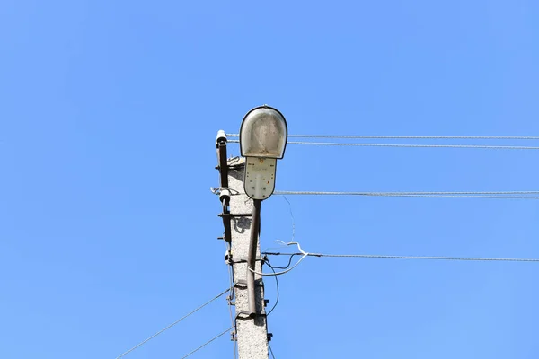 Starý betonový elektrický sloup pro přenos drátové elektřiny s lampou na pozadí zatažené modré oblohy. Zastaralé já. Typ dodávky elektrické energie — Stock fotografie