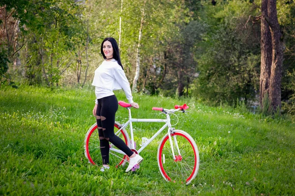Menina em uma bicicleta vermelha e branca. Um muito jovem sexy bronzeado atletismo menina passeios na natureza. morena alegre e sorridente. bons números . — Fotografia de Stock