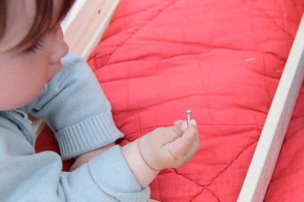 Dítě drží šroub. Detailní dětské ruce držící šroub na dřevěné desce. Lekce řemesel ve školce. Sada nástrojů na stole. — Stock fotografie