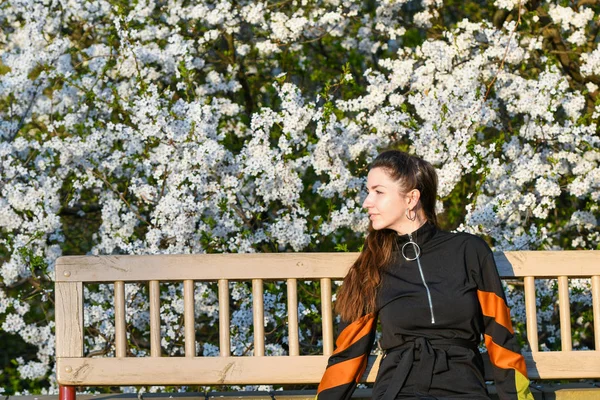 Meisje op de achtergrond van een bloeiende appelboom. in zwarte kleren. — Stockfoto