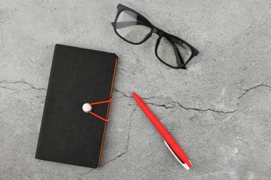Gri arka planda not defteri olan gözlükler. İş aksesuarlarıyla dolu bir ofis masası. Üst görünüm 