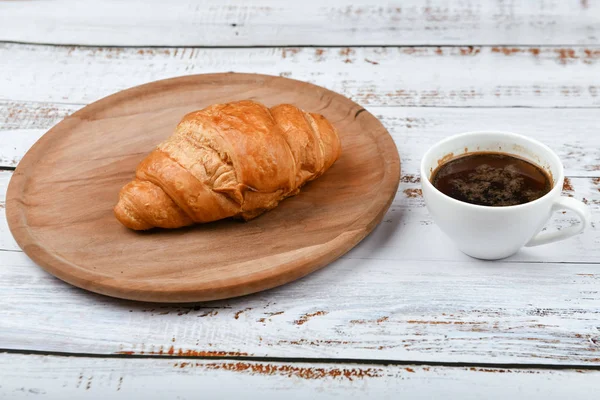 Croissant y taza de café en una mesa blanca de madera. Croissant francés fresco. sobre un fondo de madera. Vista desde arriba. Desayuno por la mañana con croissant. Desayuno francés preparado en casa. — Foto de Stock