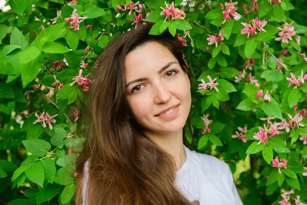 Joven chica hermosa cerca de las flores. Fotón verde y flores. Retrato de una joven hermosa chica cerca de las flores. Retrato de una joven hermosa mujer, cara bonita de cerca, grandes labios rosados, pelo liso dr — Foto de Stock