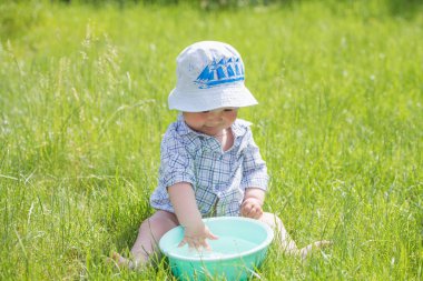 Çocuk çimlerin üzerinde bir leğen suyla oynuyor. Komik bebek dışarıda su ve baloncuklarla oynuyor. Tatlı bir erkek bebek dışarıda sabun ve suyla oynarken komik bir yüz ifadesi takınıyor.