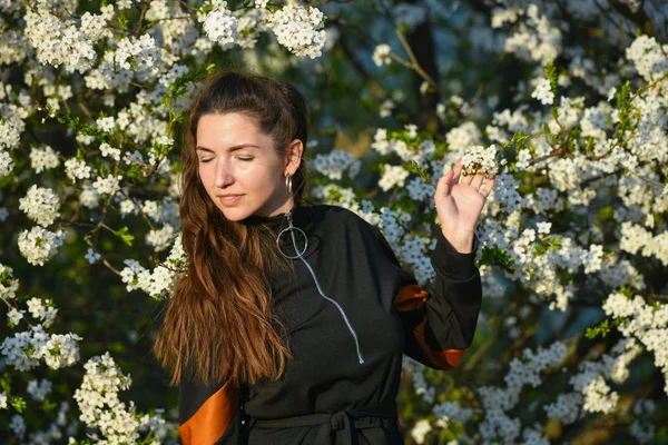 Meisje op een achtergrond van een witte bloeiende boom. Outdoor portret van jonge mooie modieuze elegante dame met lang haar, het dragen van stro hoed, vintage blouse, blauwe oorbellen, poseren in de bloeiende ap — Stockfoto