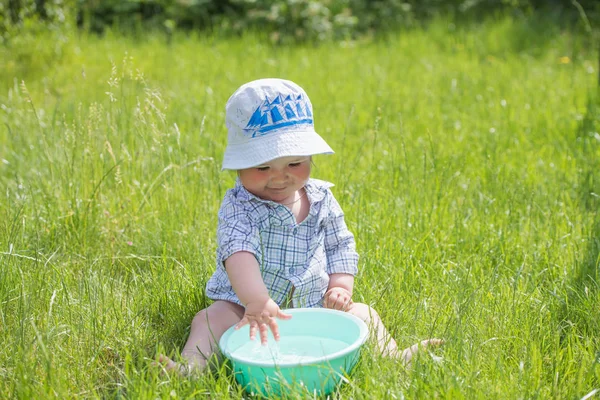 Enfant joue avec un bassin d'eau sur l'herbe. Bébé garçon drôle jouant dehors avec de l'eau et des bulles. Un petit garçon mignon fait un drôle de visage alors qu'il joue dehors avec du savon à bulles et de l'eau dans un t de lavage — Photo