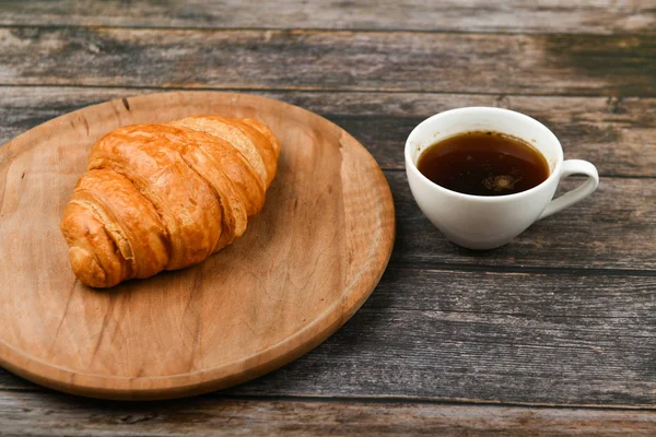 Croissant y una taza de café sobre la mesa. Croissant francés fresco. sobre un fondo de madera. Vista desde arriba. Desayuno por la mañana con croissant. Desayuno francés Excelente casero. Torre fresca. — Foto de Stock