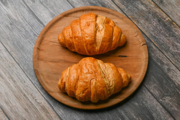 Två croissanter. Färsk fransk croissant. på en träbakgrund. Utsikt uppifrån. Morgon frukost med en croissant. Fransk frukost. Härligt hemtrevligt. Färskt torn. — Stockfoto