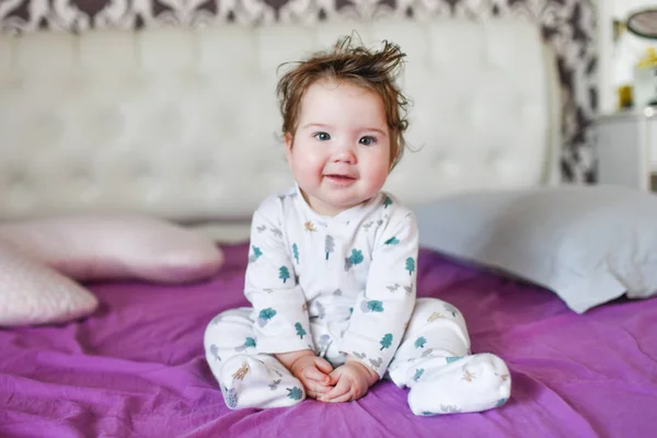 De baby zit op het bed. Leuk meisje op het bed in de slaapkamer — Stockfoto
