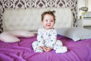 Aydınlık bir yatak odasında yeni yürümeye başlayan bir çocuk. Tatlı bir rüyadan sonra. çok renkli çarşaflar