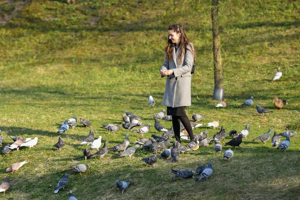 A lány madarakat etet napsütésben. Gyönyörű fiatal nő etetés madarak a parkban a napsütéses őszi napon — Stock Fotó