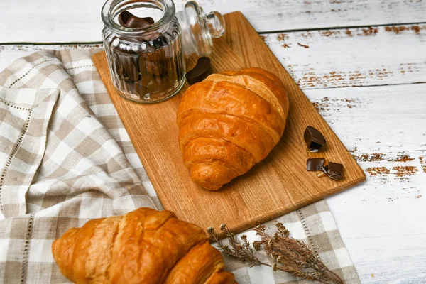 Schokoladencroissants. Der Morgen beginnt. Eine Tasse Kaffee. Frisches französisches Croissant. Kaffeetasse und frisch gebackene Croissants auf einem hölzernen Hintergrund. Blick von oben. — Stockfoto