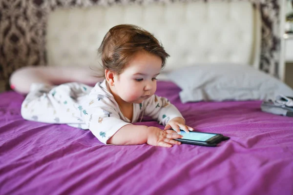 child and mobile device. Little girl in bed looking at a smartphone
