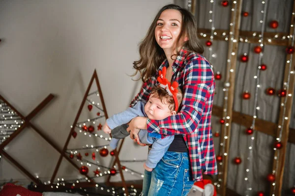 Noel geçmişinde çocuklu bir anne. Küçük bir çocuğun kafasında kırmızı boynuzlar. Yeni yıl. Noel kutlaması — Stok fotoğraf