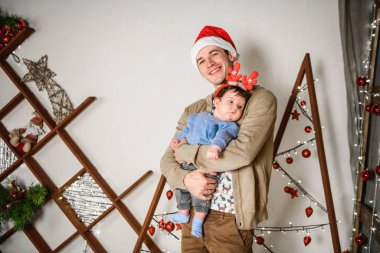 Noel geçmişinde çocuklu bir baba. Küçük bir çocuğun kafasında kırmızı boynuzlar. Yeni yıl. Noel kutlaması. Güzel bir aile Noel ağacının yanında oturur. Süveter giyen yakışıklı adam. Küçük çocuk.