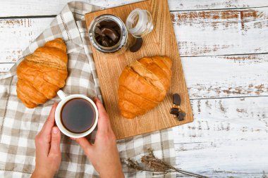 Kızın elinde kahve fincanı var. Bir kruvasanın arka planında. ay çörekli kahve. Sabahın başlangıcında. Kahve fincanı. Bir kadının elinde kahve ve taze Fransız çöreğiyle üst manzara.