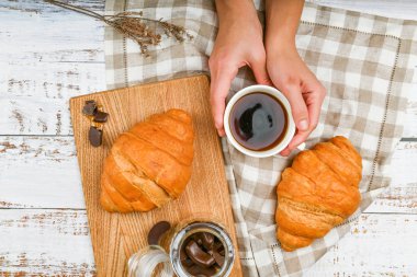 Kızın elinde kahve fincanı var. Bir kruvasanın arka planında. ay çörekli kahve. Sabahın başlangıcında. Kahve fincanı. Bir kadının elinde kahve ve taze Fransız çöreğiyle üst manzara.