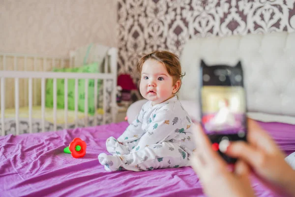 A mãe fotografa o bebé ao telefone. Mãe tira uma foto de seu bebê recém-nascido em um smartphone. Memórias familiares . — Fotografia de Stock