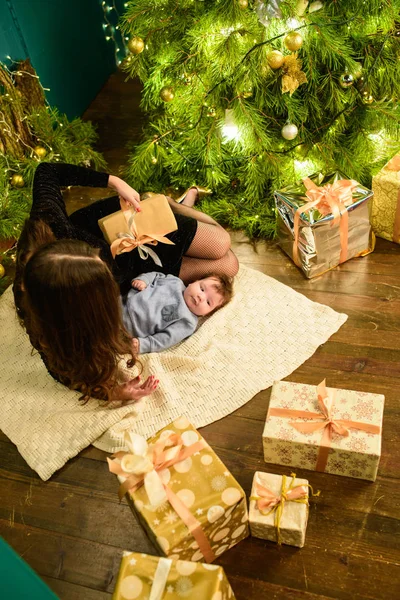 Maman et bébé s'embrassent au sapin de Noël. Happy baby et sa mère regardent le cadre. Maman avec son fils câlin pour Noël. et amusez-vous. nouveau-né pour la nouvelle année . — Photo