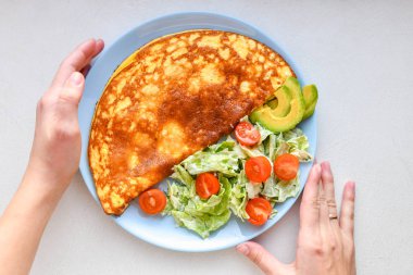 sebze ile kızarmış yumurta. çerçeveiçinde eller. Beyaz bir masa üzerinde mavi bir tabak üzerinde sebze omlet, üst görünümü