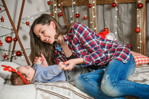 Noel arkaplanındaki bebek ve anne. Mutlu aile anne ve çocuk küçük kız oğul ve noel mucizesi. Yatakta bebeğinizle nazikçe oynuyorsunuz. Bebeğin ilk Noel 'i. Noel 'de bebek ve anne — Stok fotoğraf