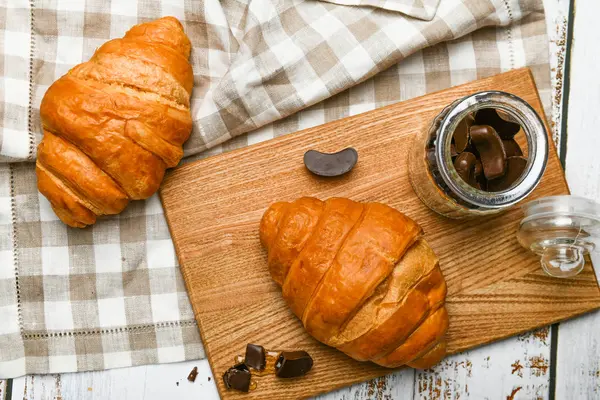 法国巧克力羊角面包的顶部视图。早上的开始。新鲜的法国羊角面包咖啡杯和新鲜烤牛角面包放在木制背景上.从上面看. — 图库照片