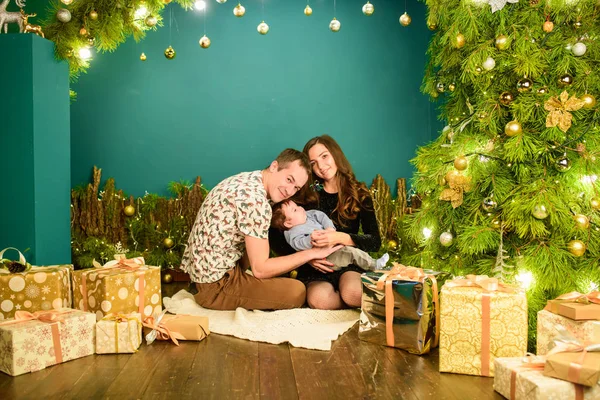 Young family at christmas time. Happy young family in christmas decorations. Mom, dad and little boy near the Christmas tree with gifts near. Family holiday. In the circle of relatives. — Stock Photo, Image