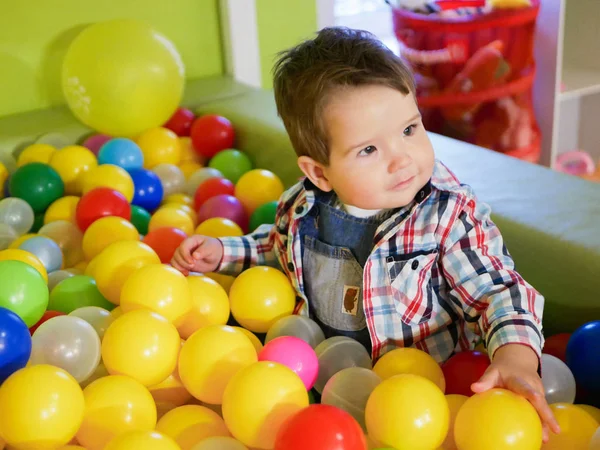 A gyerek színes golyókban játszik. műanyag labdák a játszószobában. Boldog kisfiú játszik színes műanyag labdák játszótér magas kilátás. Imádnivaló gyermek, aki jól érzi magát otthon. — Stock Fotó