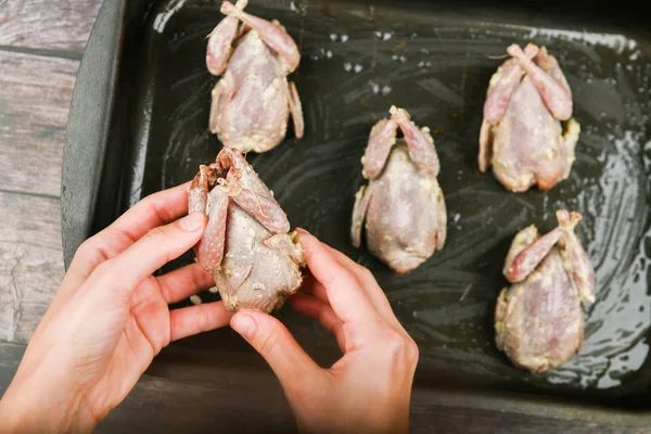 Wachtel auf einem hölzernen Hintergrund. Wachtelbacken auf einem Backblech. Wachteln kochen. Liegt auf der Stirn, vor dem Ofen. Nahaufnahme. Hände beim Kochen — Stockfoto