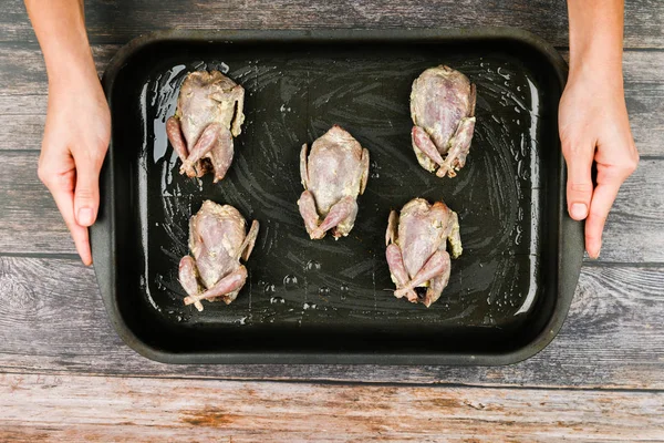 Wachtel auf einem hölzernen Hintergrund. Wachtelbacken auf einem Backblech. Wachteln kochen. Liegt auf der Stirn, vor dem Ofen. Nahaufnahme. Hände beim Kochen — Stockfoto