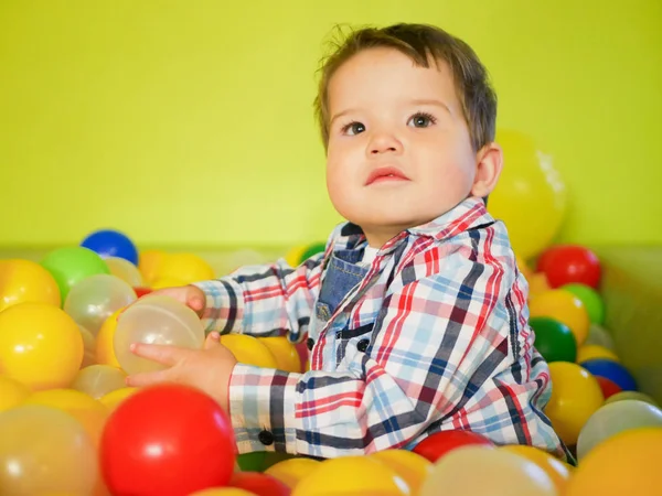 Criança joga em bolas coloridas. bolas de plástico na sala de jogos. Feliz garoto brincando em bolas de plástico colorido playground alta vista. Criança adorável se divertindo dentro de casa — Fotografia de Stock