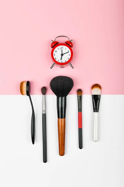 Makeup time concept. makeup brushes. Makeup cosmetics and accessories for flat lay. Composition with red alarm clock and cosmetics on a color background. Makeup concept.