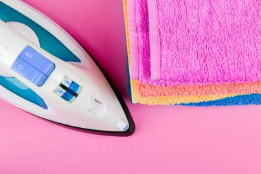 Pembe arka planda elektrikli ütü ve havlular. çok renkli havlular var. Kıyafet ütüleme konsepti. Ev düzeni