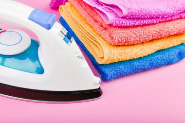 Pembe arka planda elektrikli ütü ve havlular. çok renkli havlular var. Kıyafet ütüleme konsepti. Ev düzeni