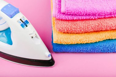 Kıyafet ütüleme konsepti. Ev siparişi. Demir ve ütülenmiş kumaş. Pembe arka planda elektrikli ütü ve havlular. çok renkli havlular..