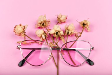 Pembe renkli gözlük. Düz yat. Cazibe ve tarz. Kadınlar için gözlük. Kurumuş güllerle süslenmiş pembe bir arka planda pembe gözlükler..