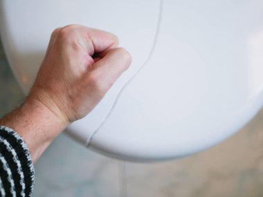 Tuvaleti yumrukla. Kırık tuvalet kapağı. Tuvalet kapağında çatlak var. Yakın plan. Kabızlık, sağlık konsepti. Tuvalette acı çekiyor. Prastatit.