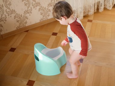 Çocuk ve lazımlık. Oturma odasında lazımlıkla oynayan sevimli bir kız bebek. Güzel bir kız bebek oturma odasında yerde lazımlıkla oynuyor. Tuvalet için çalışıyorum.