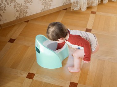 Çocuk ve lazımlık. Oturma odasında lazımlıkla oynayan sevimli bir kız bebek. Güzel bir kız bebek oturma odasında yerde lazımlıkla oynuyor. Tuvalet için çalışıyorum.