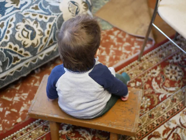 Kind im Stuhl, Rückansicht. Rückansicht eines kleinen Jungen, der auf einem alten Holzstuhl sitzt und nach unten schaut. — Stockfoto