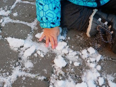 Karda bir çocuk oynuyor. 0-1 çocuk, karlı zeminde karla oynayan bir çocuk. Karlı bir parkta yürüyor, ilk karın tadını çıkarıyor.