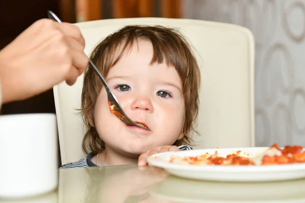 Mom feeds the baby with a fork. Mother feeds the baby. Healthy eating for kids. Parents feed the children. Family holidays, mom and son relax in a restaurant.